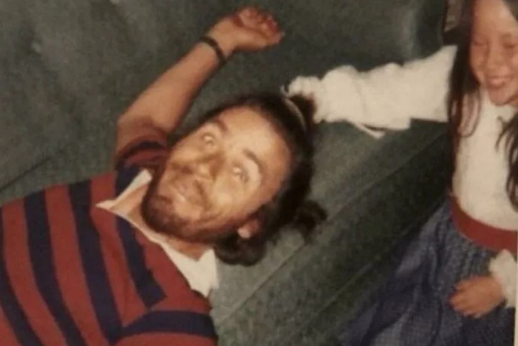 Sarjamurhaaja Ted Bundy leikkii nauravan pikkutytön kanssa sohvalla. Ted Bunty katsoo silmät ammollaan kameraan kädet levitettyinä. 