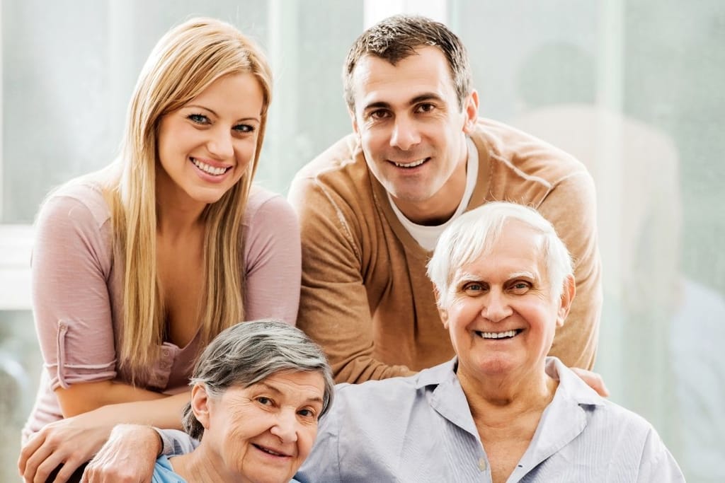 Vaalea nainen ja tumma mies istuvat iäkkäämmän pariskunnan takana. Kaikki katsovat kameraan ja hymyilevät.