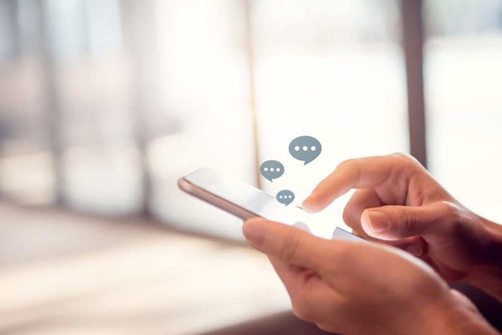 Käsi pitelee älypuhelinta kirkkaassa tilassa, ja näytön yläpuolella leijuu puhekuplia viestittelyn symbolina.