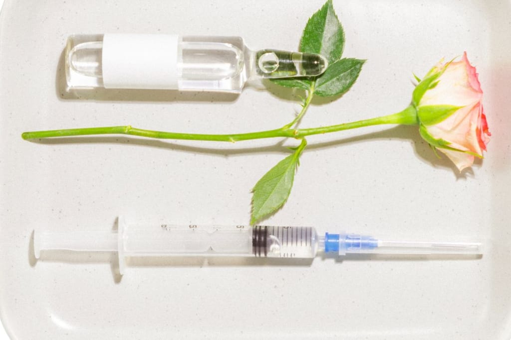 Ruusu, lasinen ampulli ja ruisku vaaleaa taustaa vasten, viitaten kauneushoitoihin ja esteettisiin toimenpiteisiin.