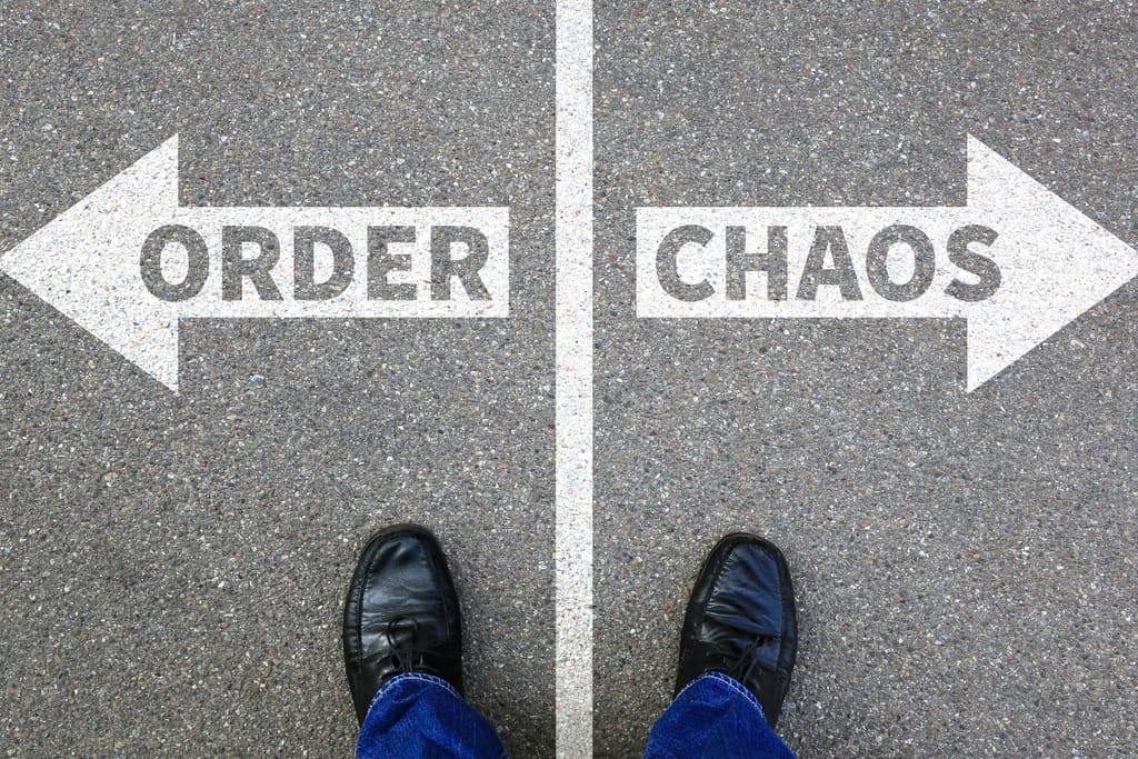 Miehen kengänkärjet osoittavat, että mies seisoo asfaltilla johon on maalattu valkoisella maalilla tienjakaja. Toisella puolella lukee järjestys, toisella kaaos. Kuva symboloi keskitietä.