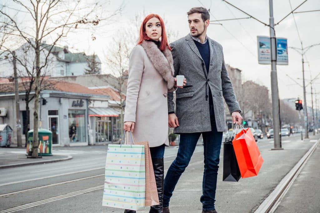 Pariskunta kävelee kaupungin kadulla ostoskassit käsissään. He katsovat eri suuntiin liikenteen keskellä.