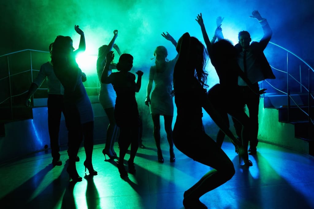 Ihmiset tanssivat yökerhon tanssilattialla värikkäiden valojen keskellä.
