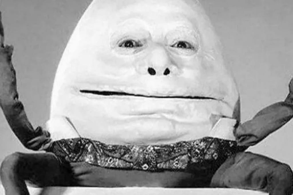 Vintagekuva kuuluisasta Liisa Ihmemaa-elokuvasta, jossa Humty Dumpty istuu koko komeudessaan. Munanmuotoinen hahmo on pelottavan näköinen ja hänen silmänsä juuri ja juuri erottuvat puvusta. Mustavalkoinen kuva. 