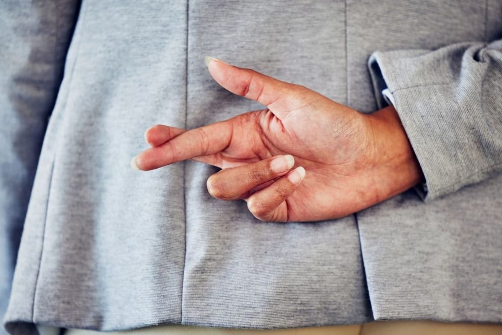 Henkilö pitää kättään selän takana sormet ristissä, ele viittaa salailuun tai epärehellisyyteen.