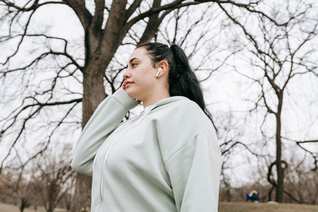 Nainen on puistossa nappikuulokkeet korvilla ja katsoo sivulle.