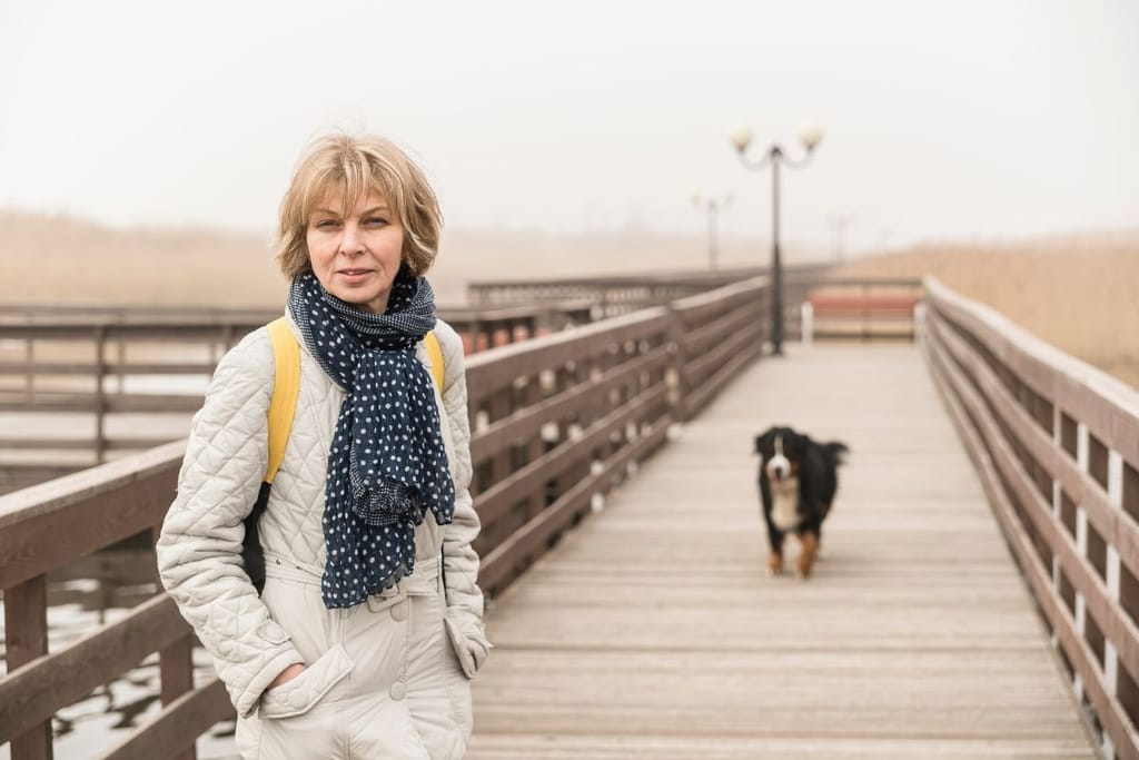 Aikuinen nainen kulkee puusillalla, taustalla kulkee koira.