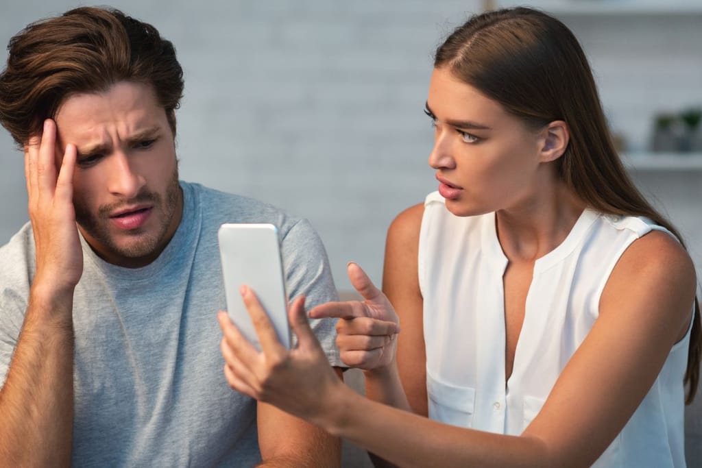 Nainen osoittaa miehen kädessä olevaa älypuhelinta, mies katsoo näyttöä huolestuneen näköisenä.