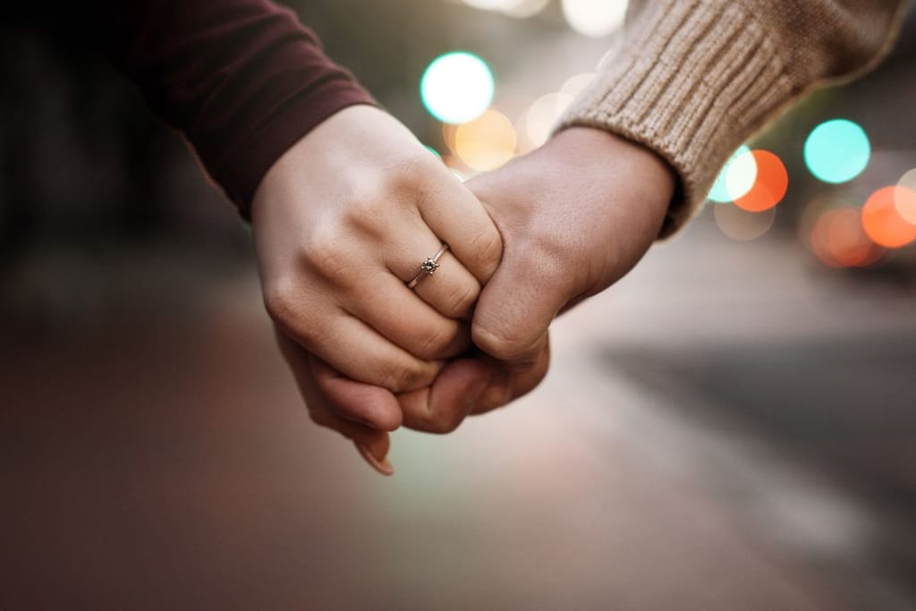 Pariskunta käsikädessä taustasta päätellen kadulla. Naisella on nimettömässään sormus, ja heidän paitojensa hihat erottuvat kuvasta. 