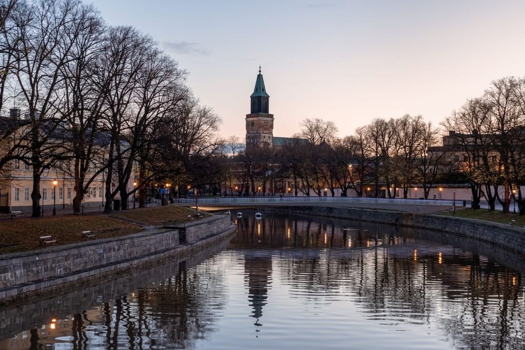 Aurajoki virtaa halki Turun keskustan, ja taustalla kohoaa valaistu Turun tuomiokirkko illan hämärtyessä.