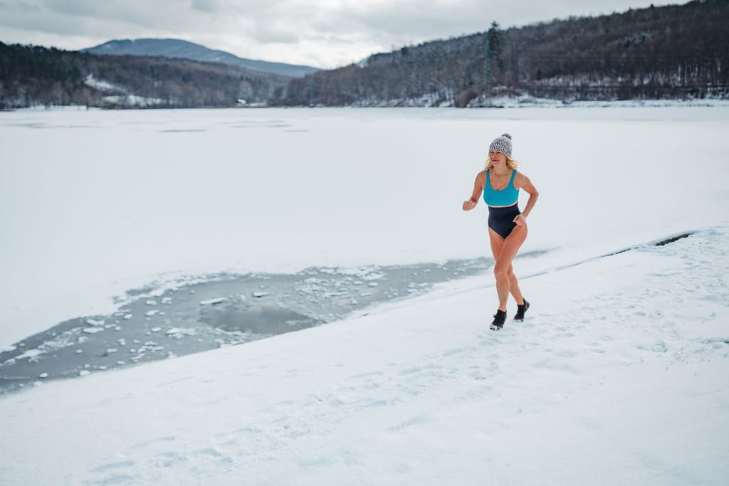 Henkilö juoksee uima-asussa lumisella järven rannalla talvimaisemassa.