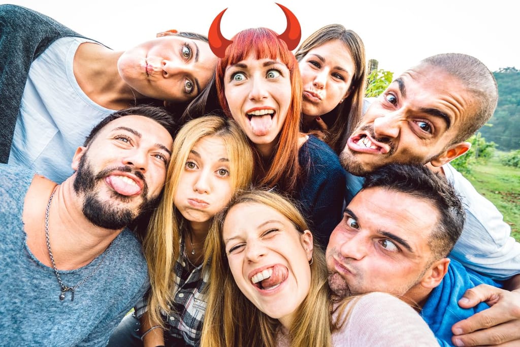 Sekaporukka, joka ilmeilee kameralle ja jokainen katsoo omaan suuntaansa. Yhdelle naiselle on piirretty pirunsarvet. 