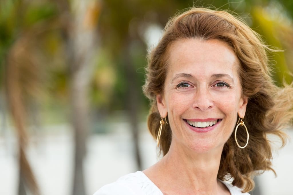 Nainen katsoo kameraan ja hymyilee ulkotilassa.