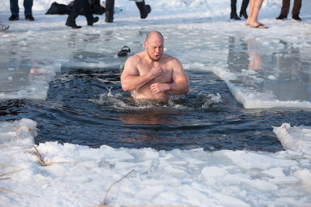 Henkilö nousee avannosta jäisessä vedessä muiden ihmisten seuratessa taustalla.