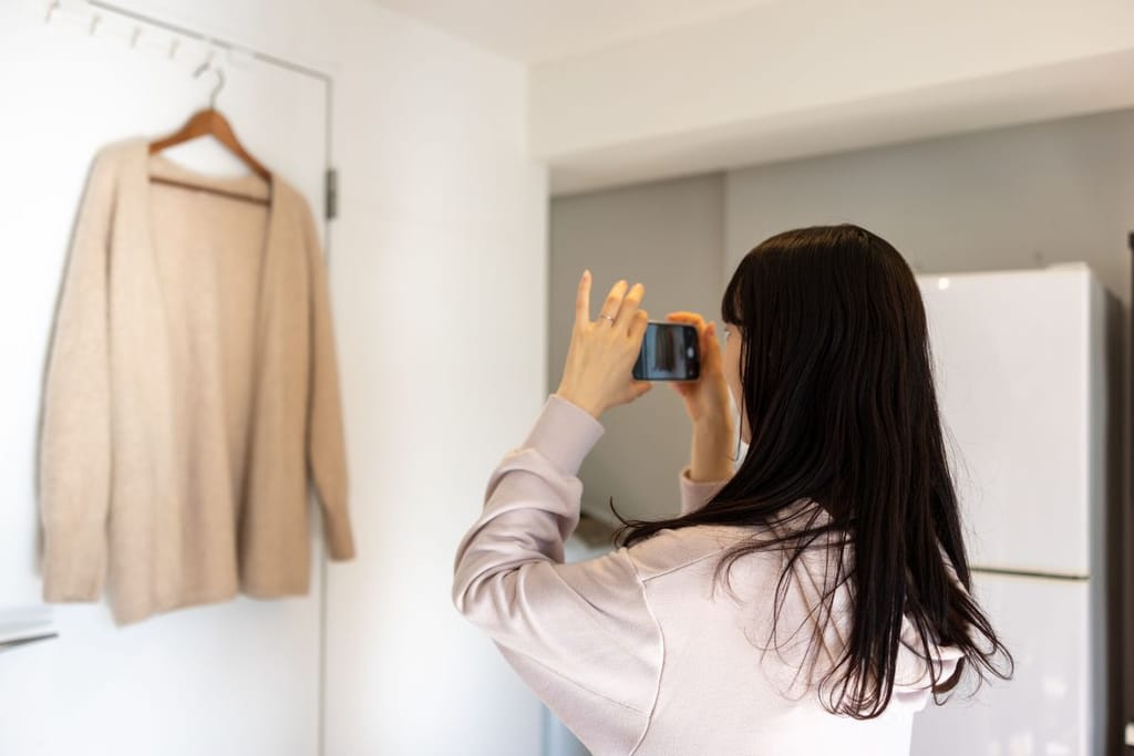 Nainen valokuvaa henkariin ripustettua paitaa älypuhelimella valkoista taustaa vasten. 