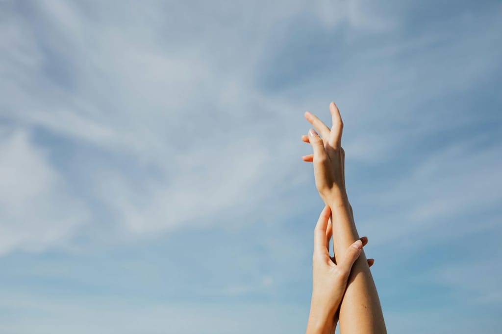 Nainen ojentaa käsiään siniselle taivaalle, jossa on ohuelti pilviä. Kuva symboloi muutosta ja uuden kaipuuta.