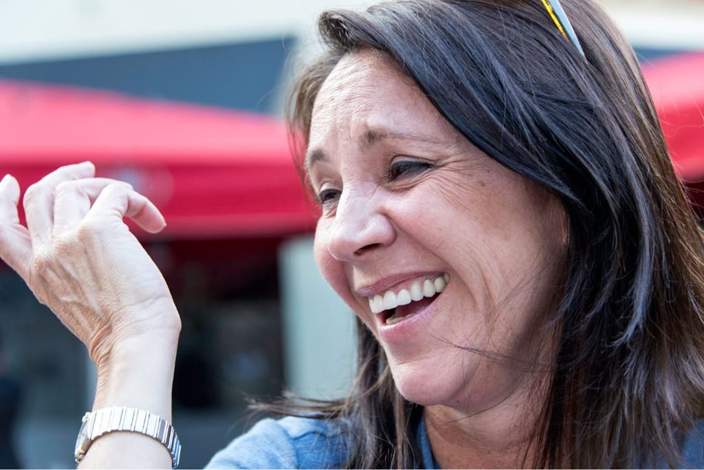 Nainen nauraa ja katsoo sivulle kaupunkiympäristössä.