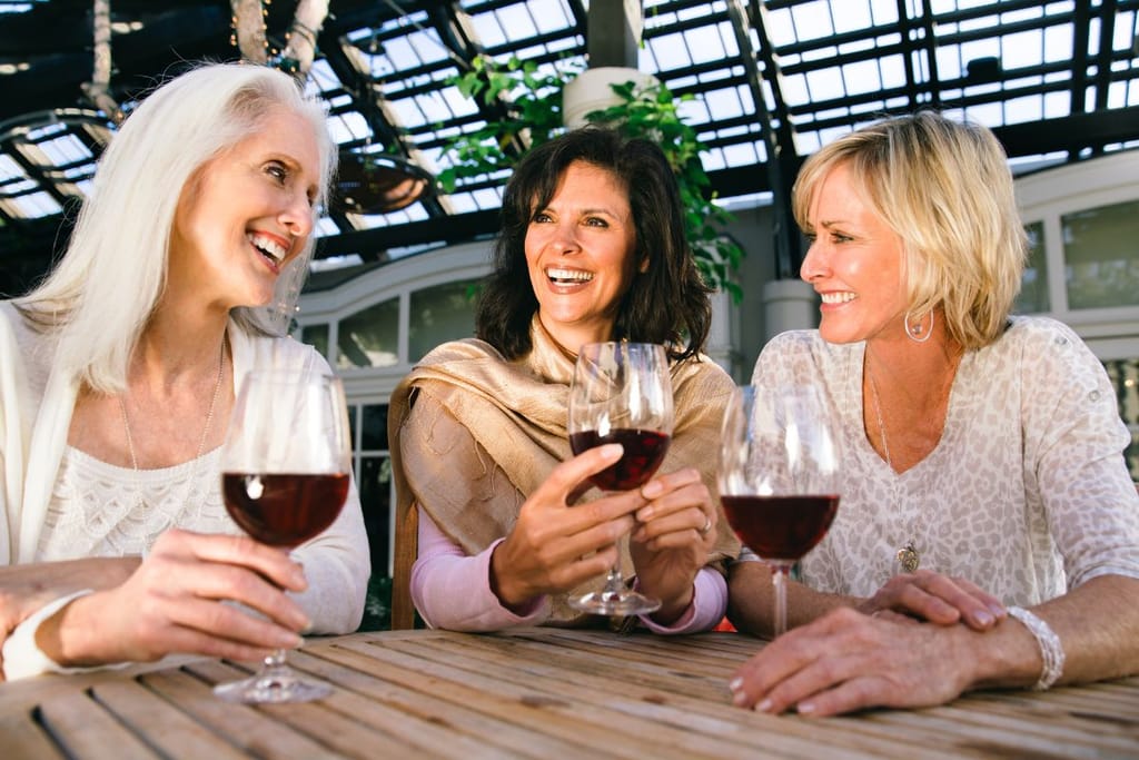 Kolme naista istuu viinilasillisilla ravintolaympäristössä. He ovat iloisia.