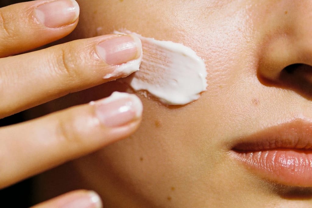Nainen levittää kasvoilleen valkoista voidetta sormillaan.
