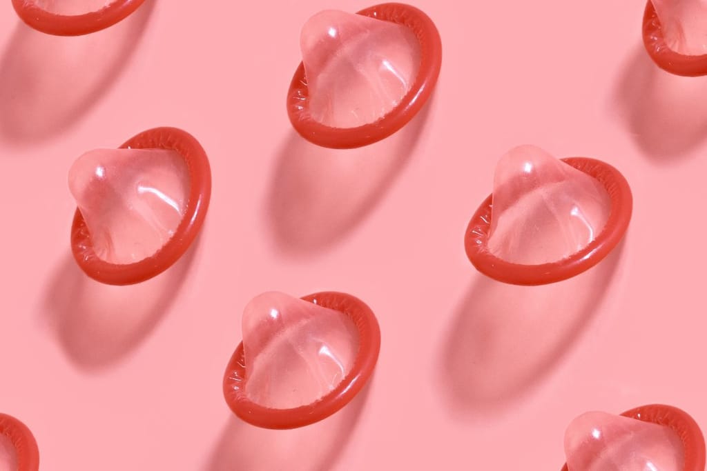 Punaisia kondomeja eli ehkäisyvälineitä vaaleanpunaista taustaa vasten. 