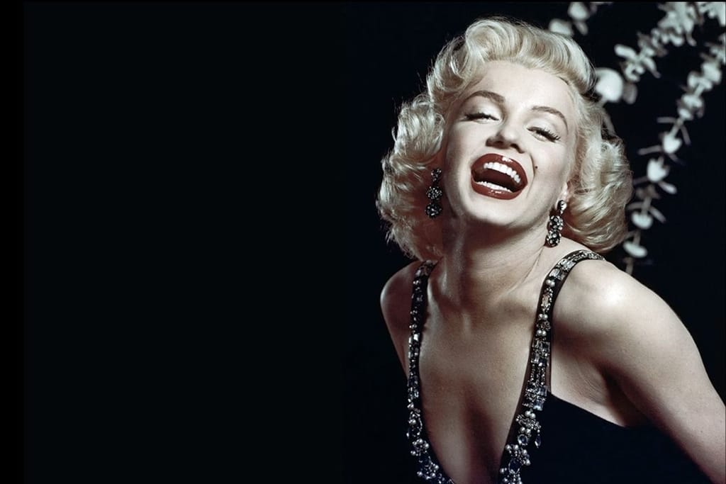Näyttelijä Marilyn Monroe hhymyilee kameralle mustaa taustaa vasten.
