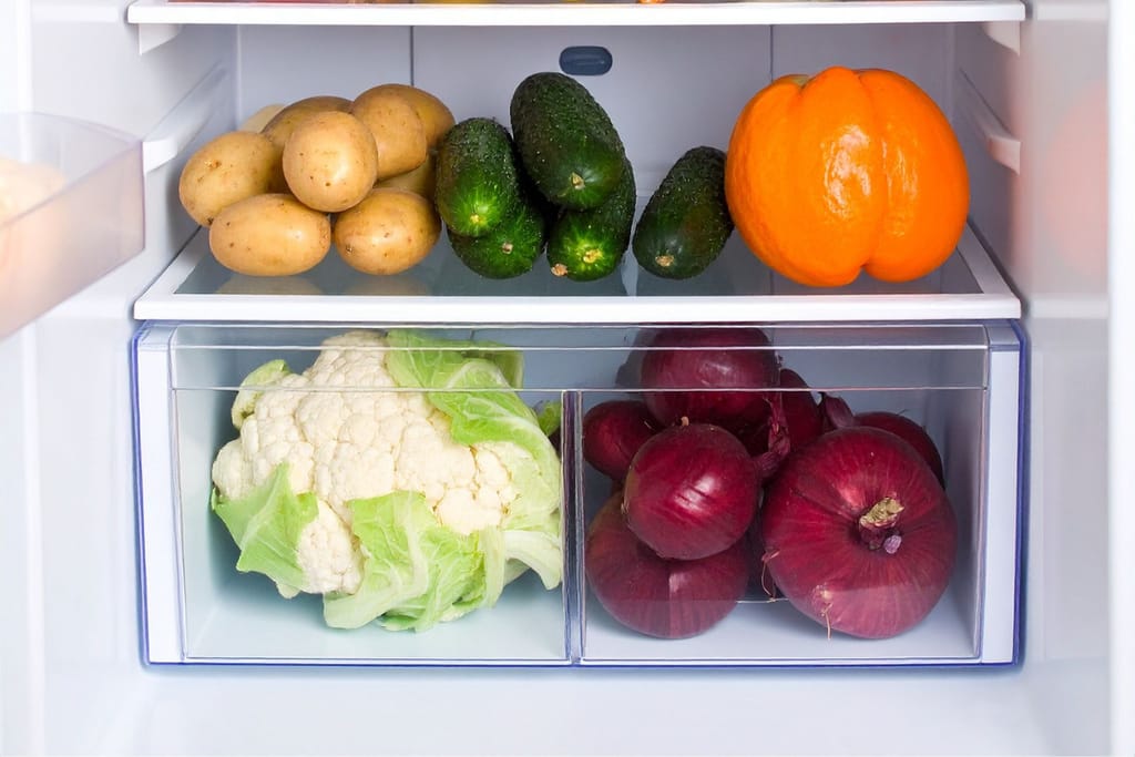Jääkaapin hyllyllä ja vihanneslaatikoissa on perunoita, kurkkuja, oranssi paprika, kukkakaali ja punasipuleita siististi järjestettynä.