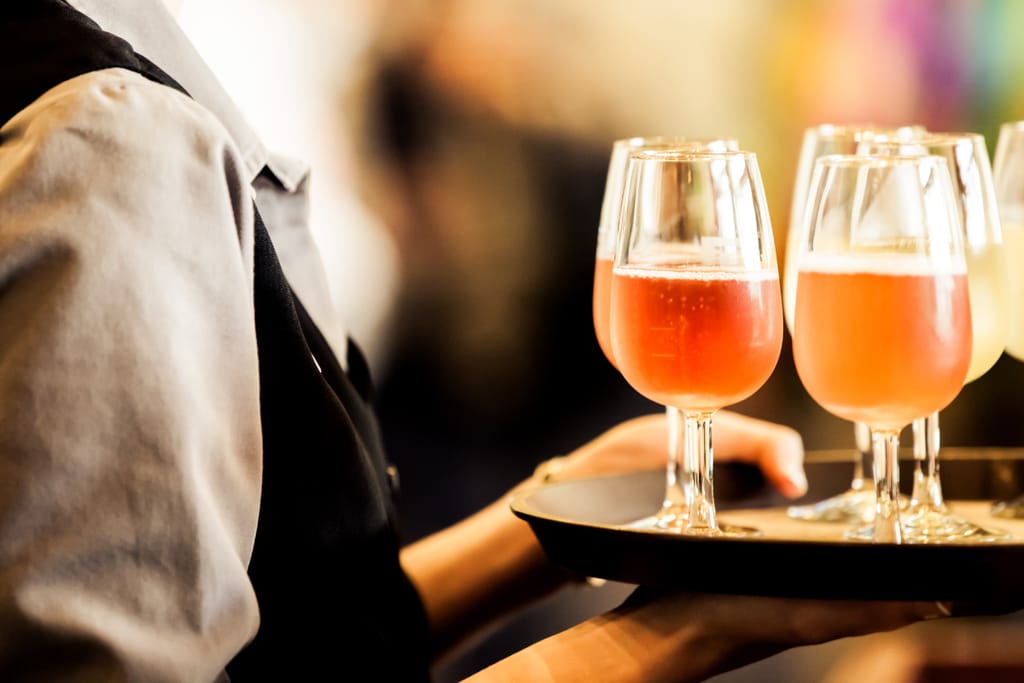 Tarjoilija kantaa tarjottimella kolmea vaaleanpunaista juomaa laseissa