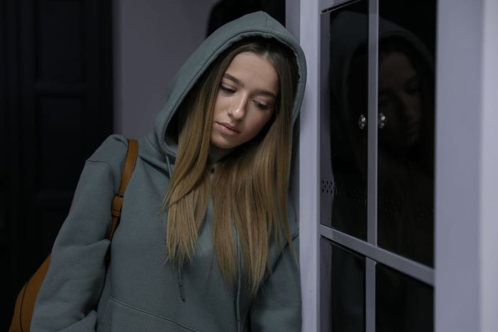 Nuori nainen huppari päässä ja hiukset olkapäillä. Hänellä roikkuu nahkareppu hartioilta ja hän nojaa oveen. 