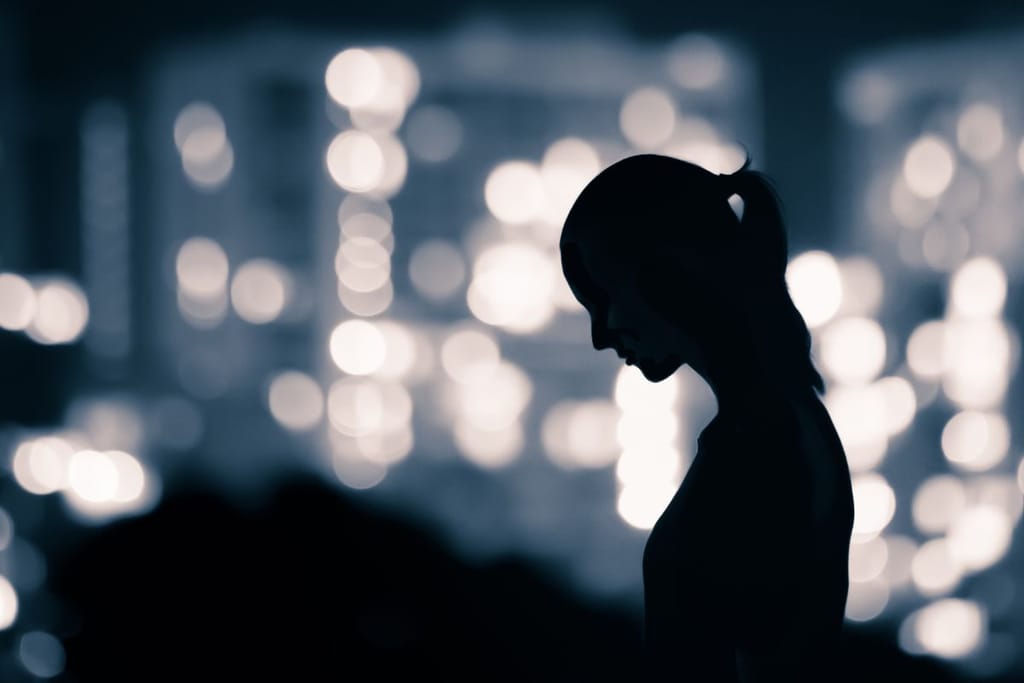 Naisen siluetti hämärässä kaupunkiympäristössä, taustalla epäteräviä valoja.
