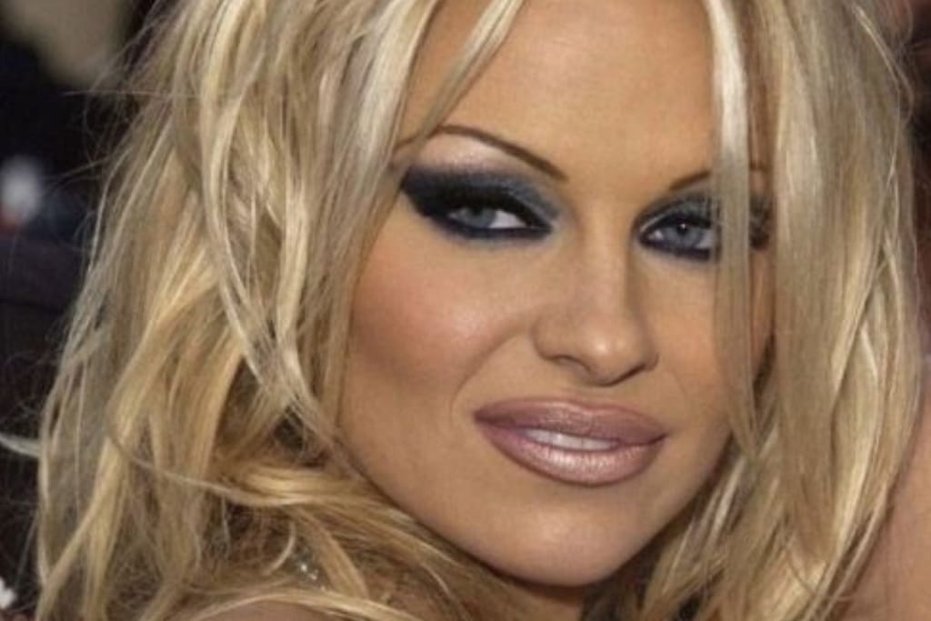 Näyttelijä Pamela Anderson poseeraa punaisella matolla nollariajan vahvassa silmämeikissä ja ohueksi nypityissä kulmakarvoissa. Kuva on tarkennettu ja rajattu erityisesti hänen kasvoihinsa.