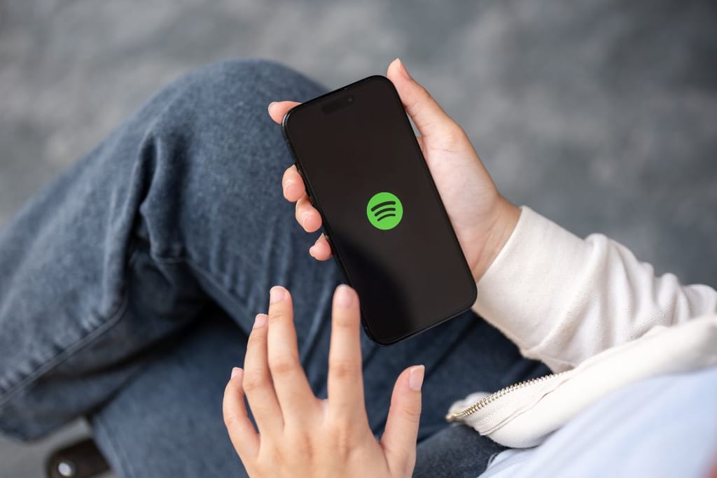 Kädet pitelevät älypuhelinta, jonka näytöllä näkyy musiikkisovelluksen vihreä logo. 