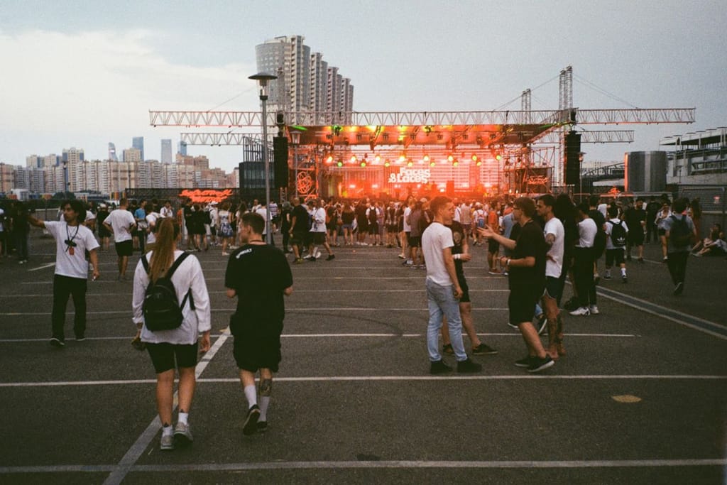 Ihmisiä ulkoilmakonsertissa festarialueella, lava valaistuna taustalla.