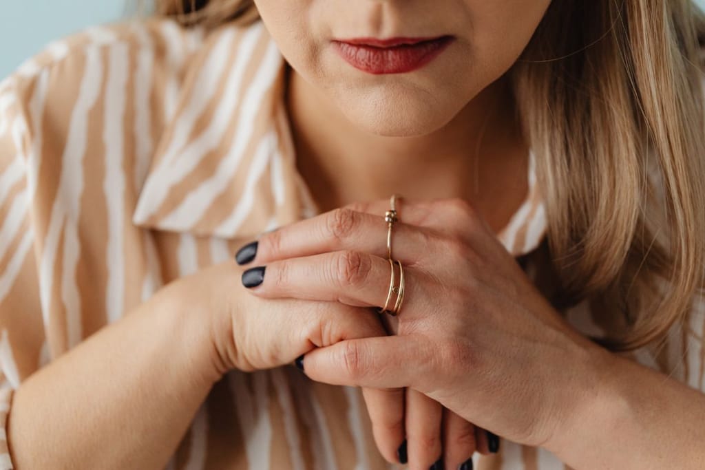 Nuoren naisen kädet ristittynä pöydällä, kasvot lähikuvassa. 