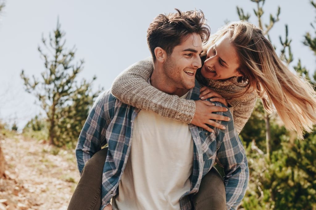 Mies kantaa reppuselässä naista luonnonkeskellä. 