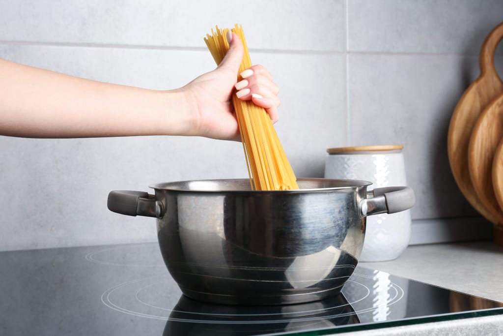 Käsi lisää spagettia kiehuvaan kattilaan keittiössä.