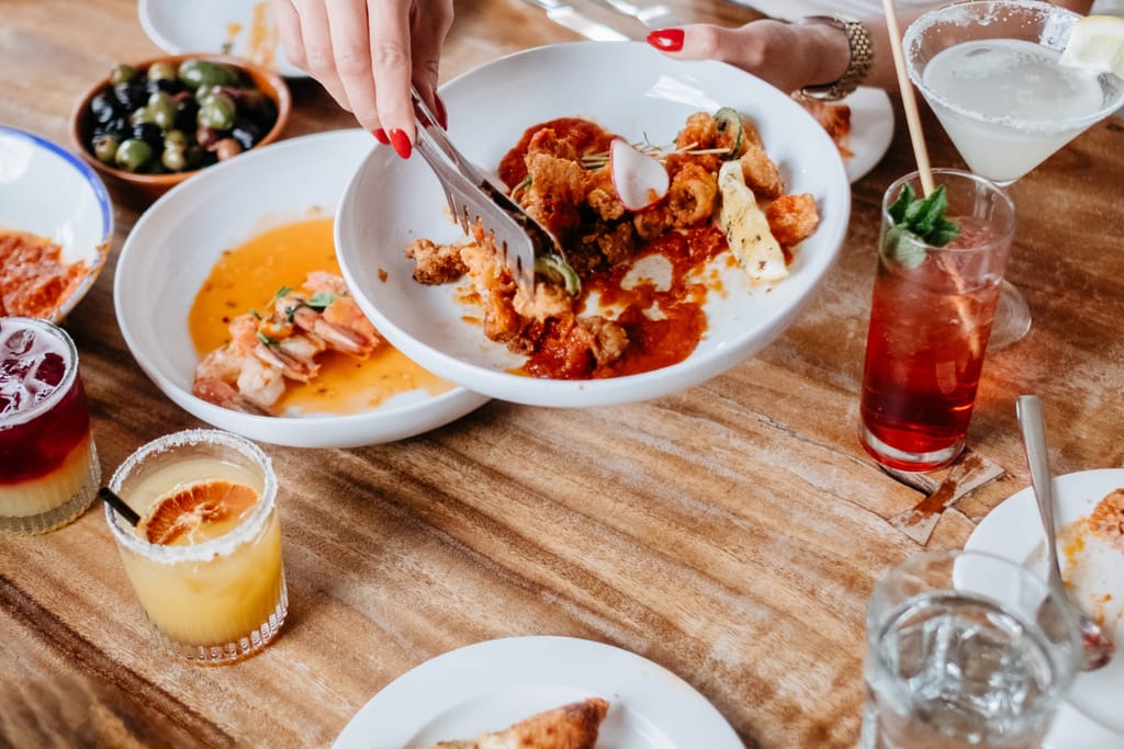 Käsi ottaa ruokaa jaettavasta annoksesta ravintolapöydässä.