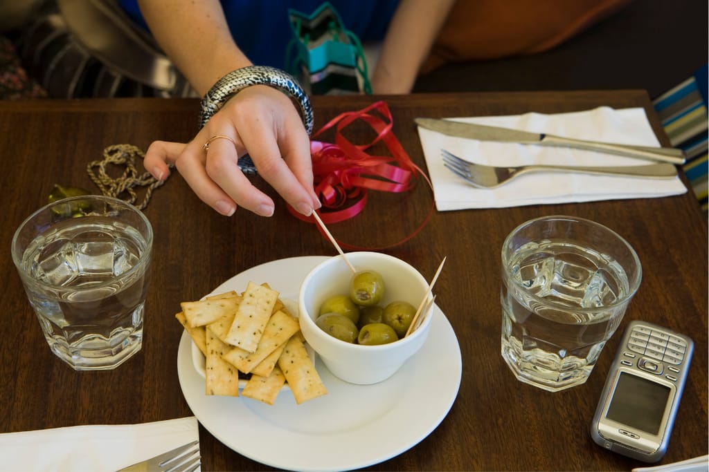 Käsi poimii vihreän oliivin kulhosta ravintolapöydässä.