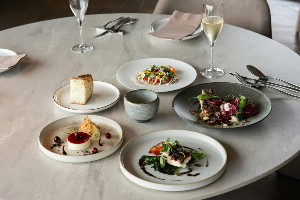 Useita ravintola-annoksia katettuna pöydälle viinilasien kanssa.