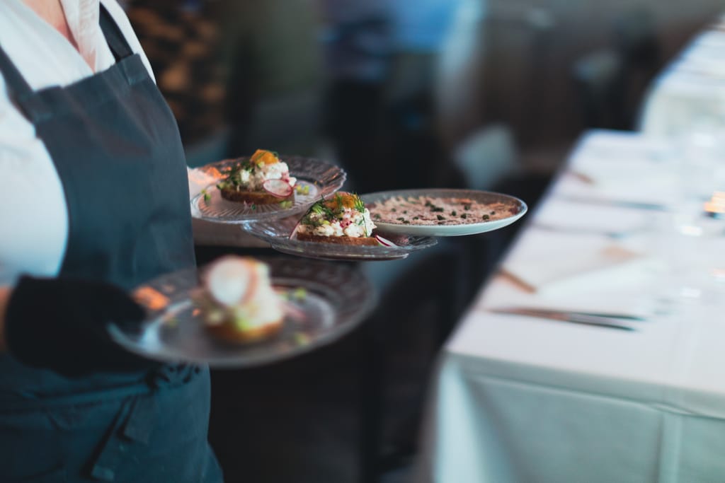 Ravintola Mamin tarjoilija kantaa useita pieniä annoksia lautasilla ravintolassa.