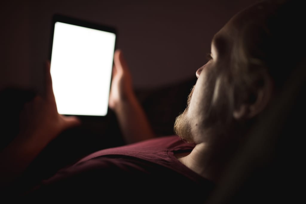 Mies makaa pimeässä ja katsoo kirkasta puhelimen näyttöä myöhään illalla.