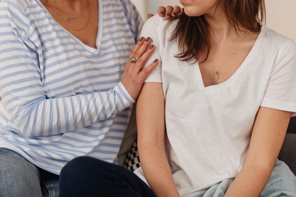Aikuinen nainen laskee kätensä toisen naisen olkapäälle lohduttavasti.