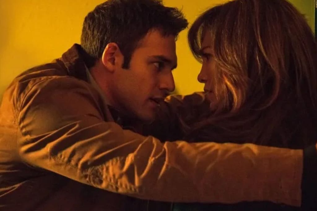 Mies ja nainen ovat hyvin lähellä toisiaan lämpimän keltaisessa valaistuksessa ja katsovat toisiaan intensiivisesti.