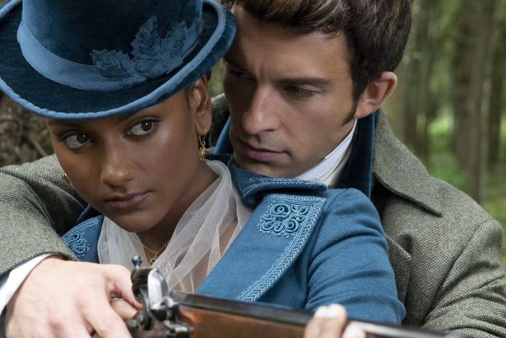 Nuori nainen sinisessä hatussa ja takissa pitää käsissään vanhanaikaista asetta, kun mies hänen takanaan ohjaa häntä läheltä metsäisessä ympäristössä.