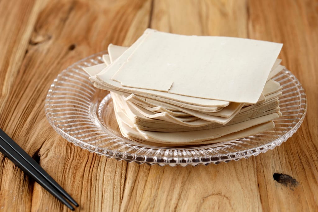 Pinottuja wonton- tai dumplingtaikinalevyjä lasilautasella puupöydällä.