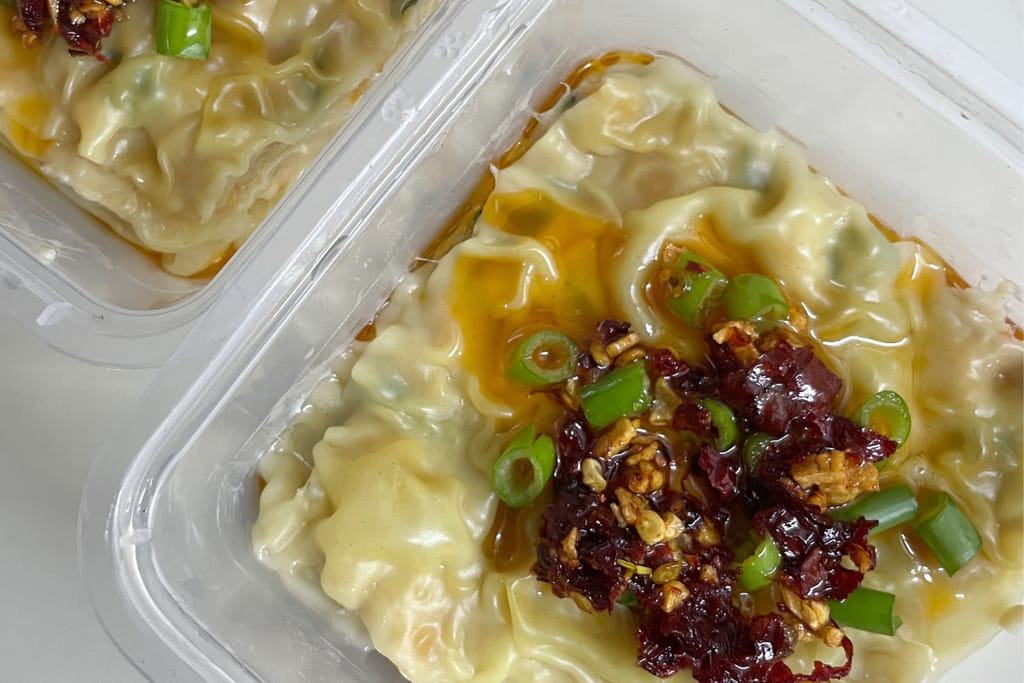 Valmis dumpling-lasagne rasiassa, päällä chiliöljyä, kevätsipulia ja rapeaa täytettä.