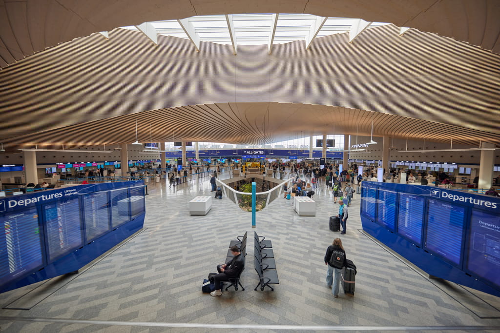 Helsinki-Vantaan lentoaseman lähtöaula ylhäältä kuvattuna, matkustajia ja suuret lähtötaulut molemmin puolin avaraa tilaa.