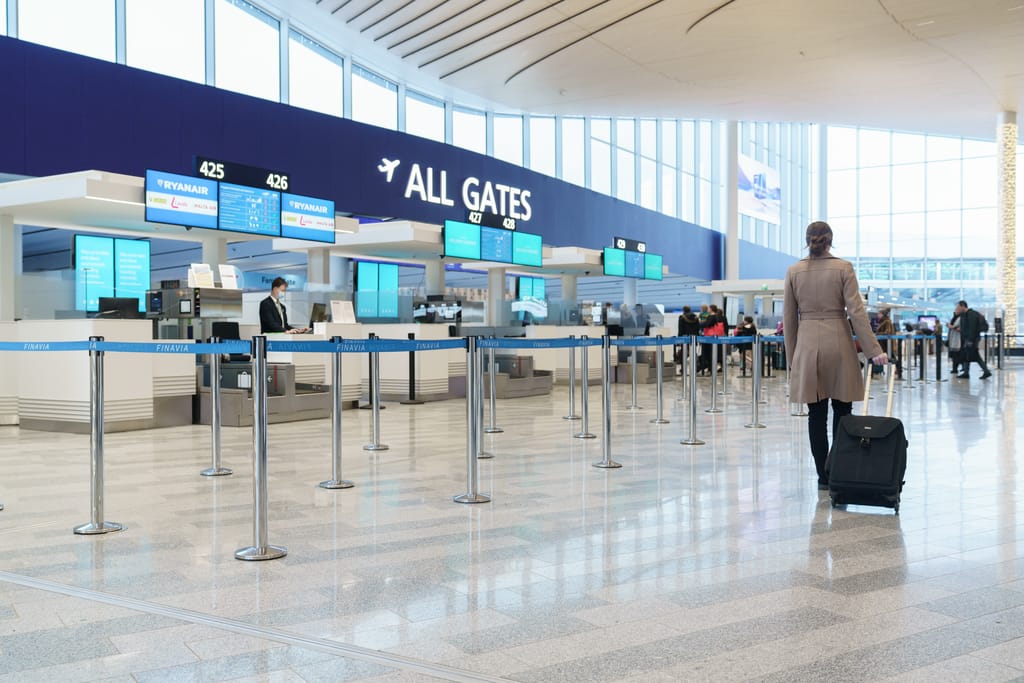 Matkustaja vetää matkalaukkua Helsinki-Vantaan lentoaseman lähtöselvitysalueella, taustalla All Gates -kyltit ja lähtöportit.