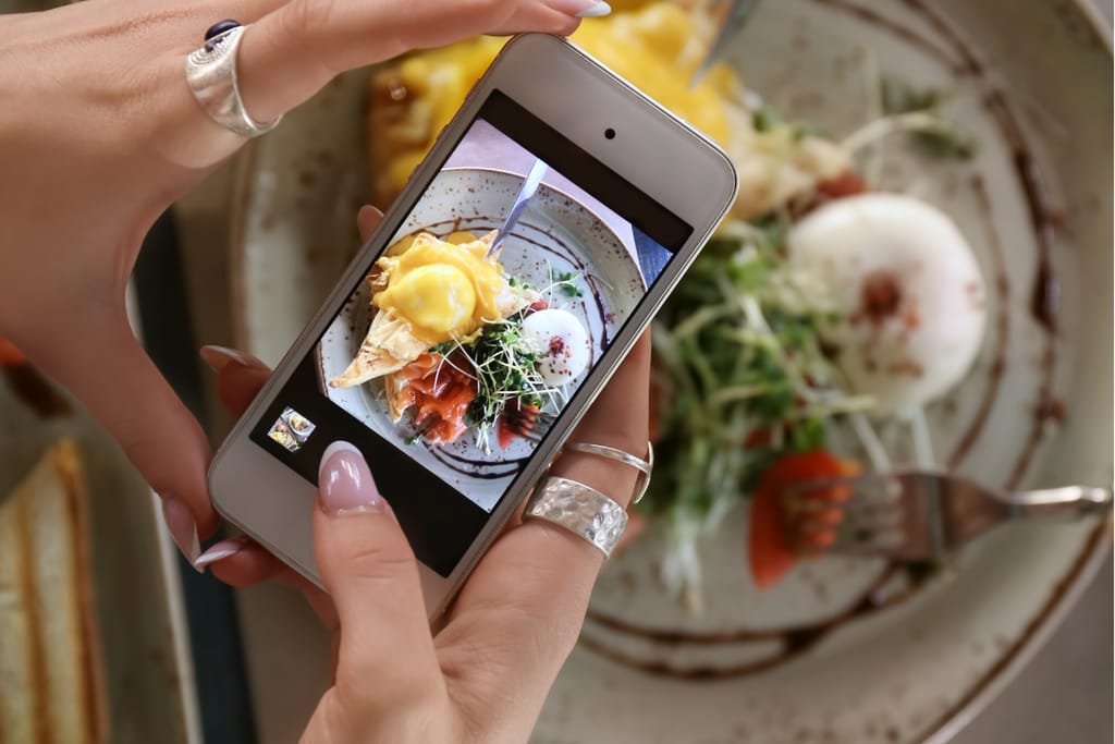 Henkilö kuvaa älypuhelimella annosta, jossa on uppomuna ja vihanneksia ravintolassa.