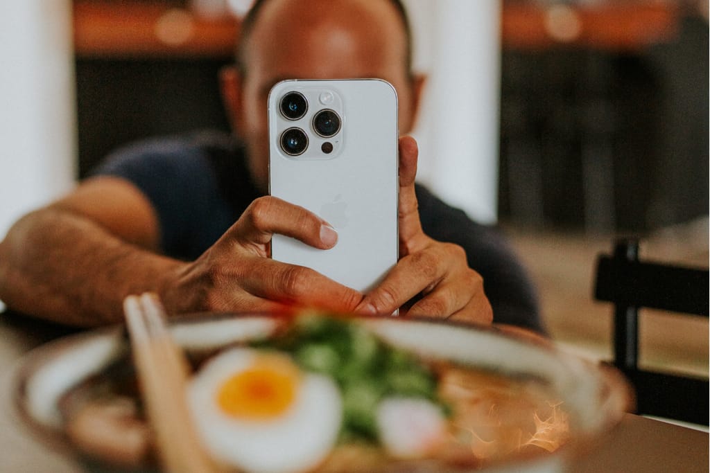 Mies ottaa älypuhelimella valokuvaa ravintola-annoksesta pöydän ääressä.