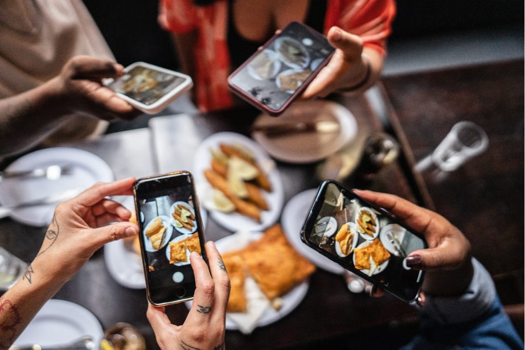 Useat ihmiset kuvaavat ruokaa älypuhelimilla ravintolapöydän ääressä ennen syömistä.